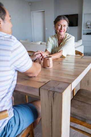 Diverse Couple Holding Hands at Wooden Dining Table in Cozy Living Room