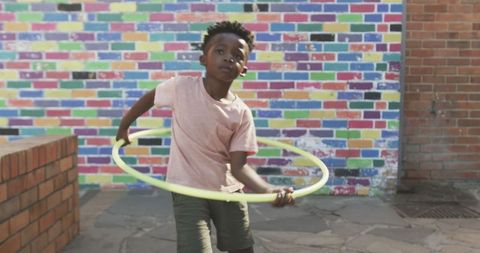Playful child spinning hula hoop in multicolored urban courtyard