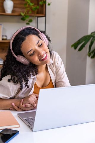 African american woman wearing pink headphones working from home on laptop in cozy study