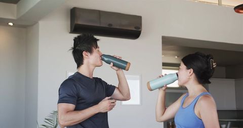 Couple hydrating after home workout drinking matching reusable bottles fitness lifestyle