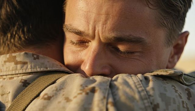 Soldier embracing comrade, pressing face into shoulder in desert sun, military reunion
