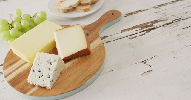 Cheese presentation on wooden board with different cheese types, green grapes, and sliced bread in background. Perfect for illustrating concepts of gourmet food, dinner parties, appetizers, farmhouse-style serving, brunch setups, or food photography.