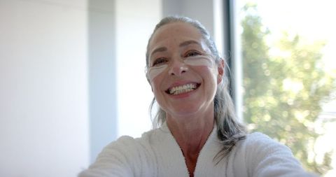 smiling mature woman in bathrobe with eye patches embracing self-care - Download Free Stock Images Pikwizard.com