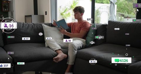 Young man reading on sofa with floating social media notifications and likes