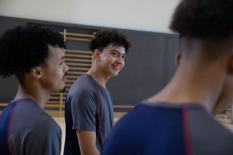 Diverse teen teammates smiling and chatting in school gym during practice