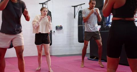 Diverse group practicing boxing guard and footwork on pink gym mats in training class
