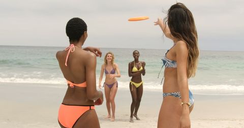 group of diverse women playing frisbee on sandy beach near water. captures joy and companionship of friends, highlighting their happiness. perfect for advertisements about travel, vacations, or summer activities, or use in publications celebrating diversity and friendship.