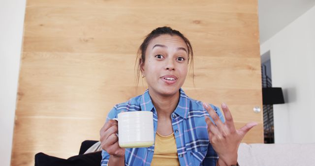 Young woman enjoying coffee at home while engaging in conversation. Ideal for use in lifestyle blogs, social media posts about home life and relaxation, personal anecdotes, and promotional material for coffee brands.