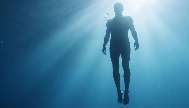 Male silhouette floating underwater with sunbeams and bubbles, serene deep sea solitude