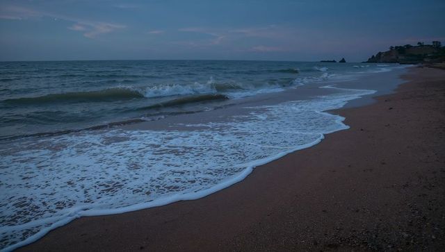 Dusk shoreline with rolling surf and foamy waves curving along sandy pebble beach