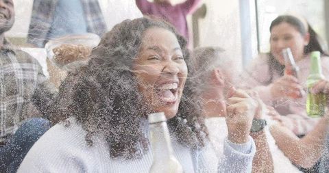 Laughing woman celebrating with friends on sofa raising fists and holding bottled drinks