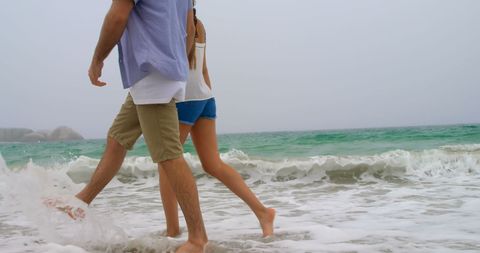 Young Couple Enjoying a Walk on Sandy Beach with Crashing Waves