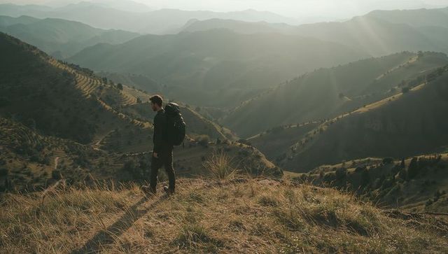 Male hiker standing on ridge overlooking layered mountain valleys at golden hour