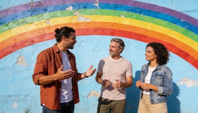 Friends chatting under rainbow mural on peeling urban wall, sunlit casual conversation
