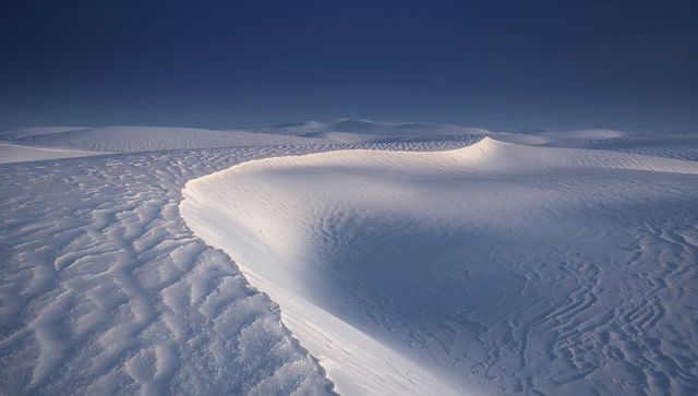 Curving white sand dune crest sculpting wind-rippled gypsum desert under deep blue sky