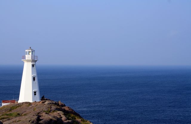 Solitary white lighthouse standing on rocky coastline by calm blue ocean - Download Free Stock Images Pikwizard.com