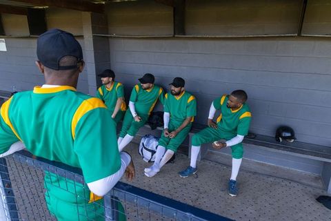 Baseball team resting and strategizing in dugout wearing green uniforms and white socks
