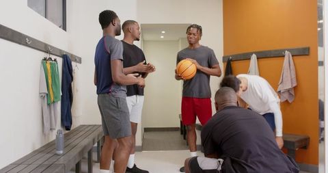 Young basketball teammates chatting in locker room holding basketball during pregame routine
