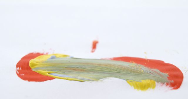A smear of red and yellow paint blends on a white background, creating an abstract design with copy space. Artistic expression is captured in the vibrant streaks, suggesting movement and creativity.
