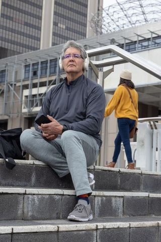 Senior man sitting on city steps listening to headphones urban lifestyle portrait