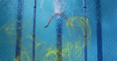 Male swimmer kicking underwater with yellow dye clouds in lap pool