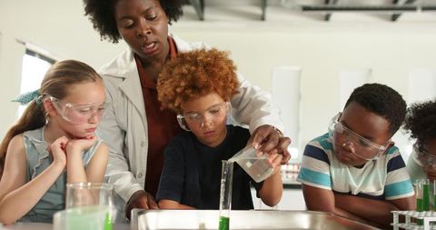 African american teacher guiding diverse children conducting hands-on chemistry experiment in classr