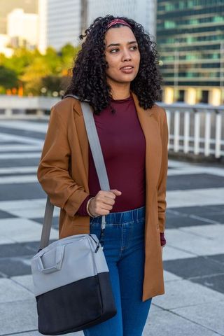 Urban young woman walking with tote bag in business casual coat during golden hour