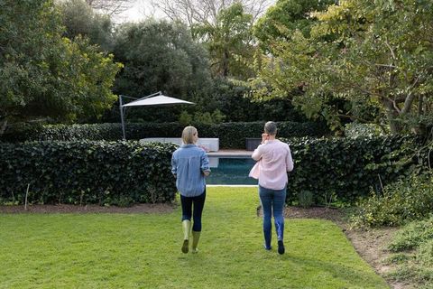 Middle-aged women walking toward backyard pool wearing rubber boots and chatting