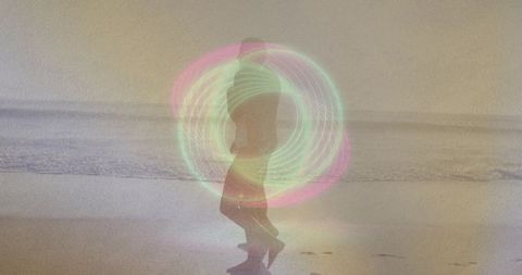 Double-exposing couple creating led hoop neon light circles on beach shoreline at dusk