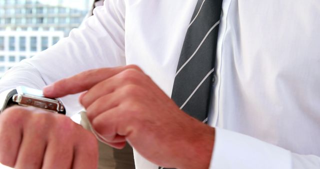 A close-up of a businessman wearing business attire while using a smartwatch outdoors. Perfect for themes around business technology, time management, productivity, modern work environments, and professional life.