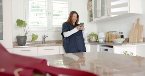 Smiling Female Doctor Using Smartphone in Modern Kitchen