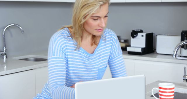 Happy woman doing her accounting with laptop in the kitchen