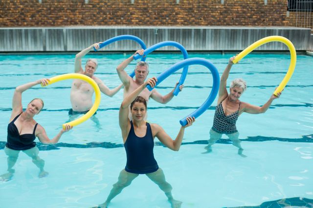 Female trainer and senior swimmers exercising with pool noodle