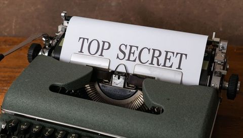 Vintage green typewriter bearing top secret document on wooden desk closeup