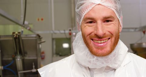 Smiling butcher in hygiene gear at meat processing facility