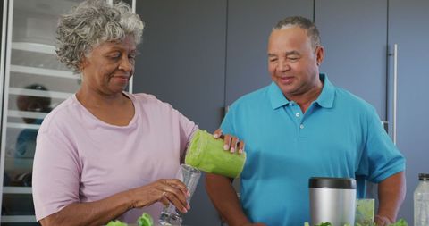 Senior couple preparing healthy green smoothie in modern kitchen