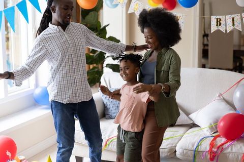 Diverse family celebrating child's birthday at home with balloons, streamers, and smiling faces