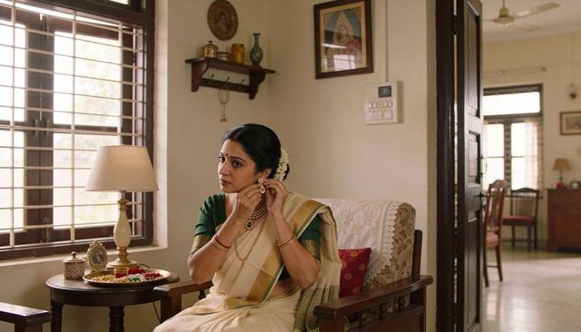 Indian woman adjusting earring wearing cream saree and green blouse in traditional home