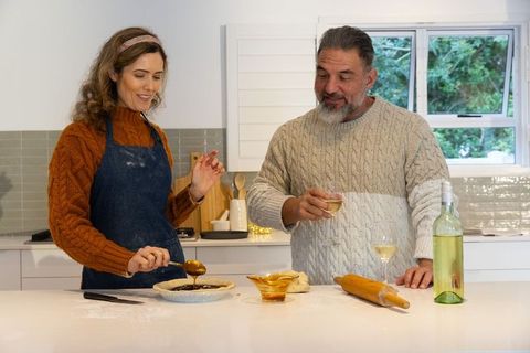 Couple baking pie together in bright kitchen sharing wine and rolling dough