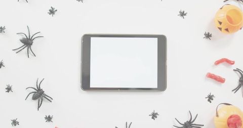 Tablet with blank screen framing halloween spiders, pumpkin pails and gummy fingers