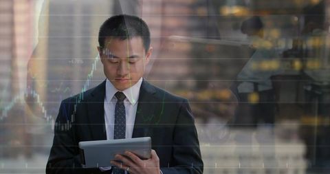 Asian businessman analyzing market charts on tablet with financial data overlay in city