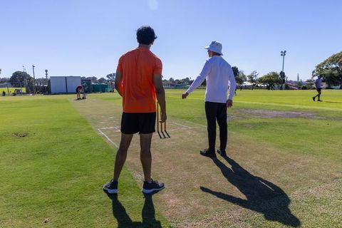 Cricket coach guiding batsman holding stumps on sunny practice pitch outdoor training