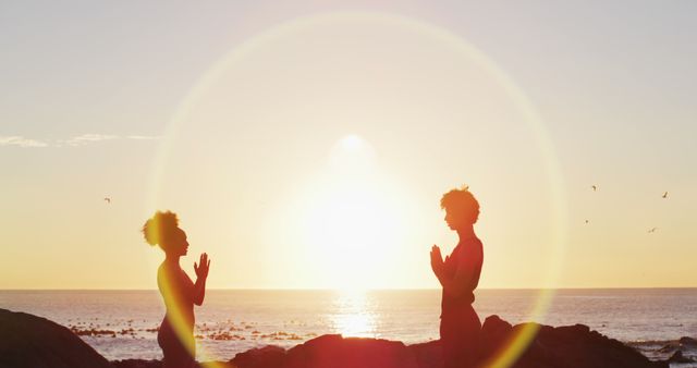 Silhouetted couple practicing yoga at sunset at beach. Togetherness and peaceful connection with nature and self. Ideal for wellness, meditation, mind-body balance, and travel themes.