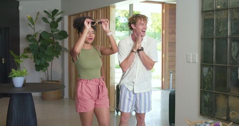 Young couple arriving home, reacting with excitement in sunlit modern entryway with luggage