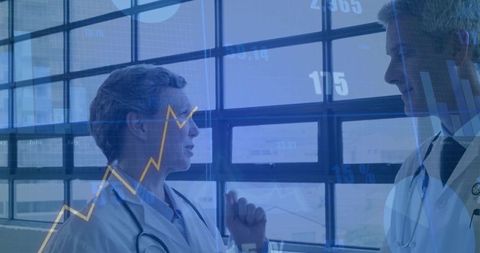 Two doctors discussing clinical analytics with digital graphs overlaying hospital window