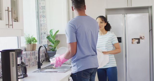 Interracial couple washing dishes together in a bright, modern kitchen. Man and woman showing teamwork and household cooperation. Ideal for use in advertisements, blogs about domestic life, household products, or promoting family bonds.