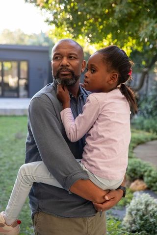 African american father holding daughter in sunlit backyard embracing family bond