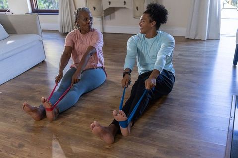Senior african american duo exercising with resistance bands on sunlit living room floor