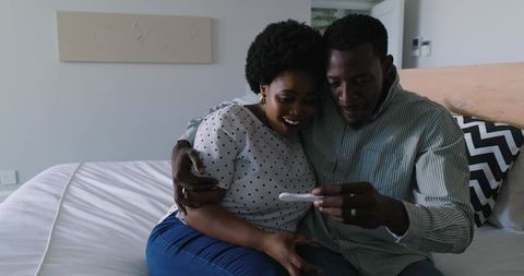 African american couple celebrating positive pregnancy test embracing surprise on bed
