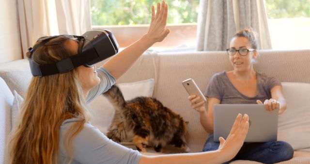 Woman Using VR Headset with Friend on Sofa Working with Laptop - Download Free Stock Images Pikwizard.com